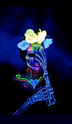 a woman's face painted with neon paint and flowers on her head, in the dark