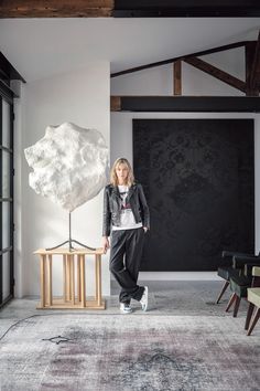 a woman standing in front of a large rock on top of a wooden table next to a chair