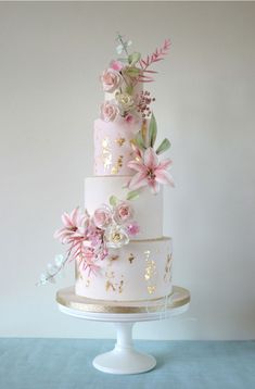 a three tiered wedding cake with pink flowers on the top and gold trimmings