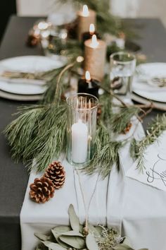 the table is set with pine cones, candles and greenery for a festive look