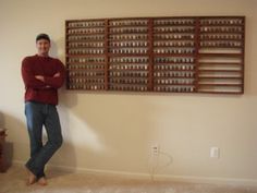 a man standing in front of a wall with many cups on it and his arms crossed