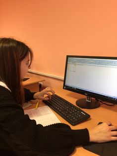 a woman sitting at a desk with a computer monitor and keyboard in front of her