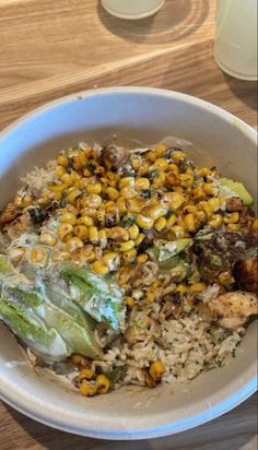 a white bowl filled with rice, corn and lettuce on top of a wooden table