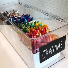 a container filled with crayons sitting on top of a white counter next to a sign