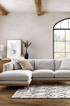 a living room with a large sectional couch and wooden table in front of the window