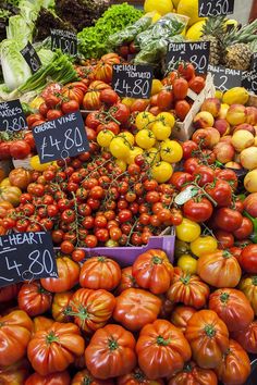 many different types of tomatoes and other vegetables on display at a market stall with price signs