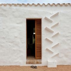 a pair of sandals sitting in front of a white building with wooden shutters and open door