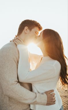 a man and woman kissing in front of the sun with their arms around each other