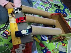 a child is playing with toy cars on a tablecloth covered floor and in front of a cardboard box