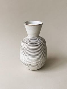 a white vase sitting on top of a table next to a gray wall and floor