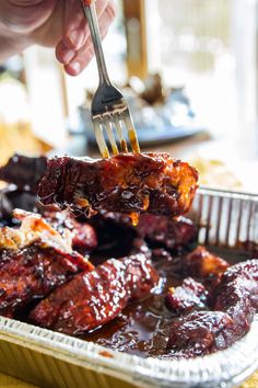 a person is holding a fork over some ribs