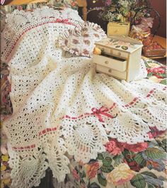 a white crocheted blanket on top of a bed next to a box and flowers