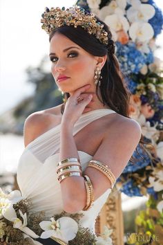 a beautiful woman in a white dress with flowers on her head and bracelets around her neck