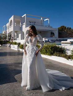 a woman in a white wedding dress standing on the ground near a building with an ocean view