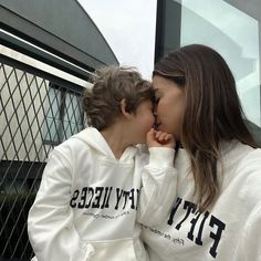 two people kissing each other while wearing white sweatshirts and black lettering on their hoodies