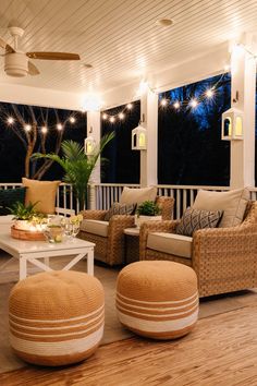 a living room with couches and chairs on the porch at night, lit by string lights