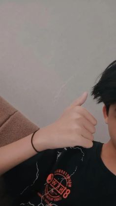 a young man with black hair giving the thumbs up sign