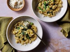 two white bowls filled with pasta and spinach on top of a pink tablecloth