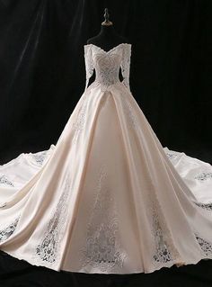 a white wedding dress on display in front of a black background with an embroidered skirt