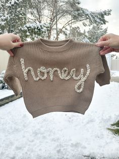 "This listing is for one personalized, hand embroidered baby name / word sweater. These sweaters are the cutest for a baby announcement, baby shower, gender reveal, family photos, 1/2 or 1st birthday and everything in between! They also make the cutest gift! **This listing includes free shipping! I currently offer up to 8 letter names/words on these sweaters. If you would like to do one word or name on top of the other, please say so in the personalization section. Please message me if you are needing more than 8 letters on the sweater. If there is an i in the name, please specify if you would like the dot to be a heart, flower or normal dotted i. These sweaters come in two sizes: 6 month and 12 month. They are made to be chunky and oversized. The 6 month currently comes in all listed colo Cute Winter Sweater With Letter Embroidery, Customizable Cute Winter Sweater, Cute Winter Sweater With Embroidered Text, Cute Customizable Winter Sweater, Embroidered Winter Birthday Sweater, Gender Reveal Family, Honey Sweater, Letter Names, Kid Outfits