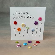 a happy birthday card with buttons and flowers on the front, surrounded by small pins