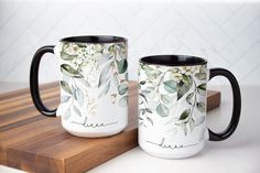 two black and white coffee mugs sitting on top of a cutting board next to each other