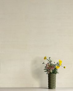 a green vase with yellow and pink flowers in it on a white table next to a wall