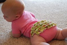 a baby laying on the floor wearing a pink shirt and green ruffle bloomed diaper