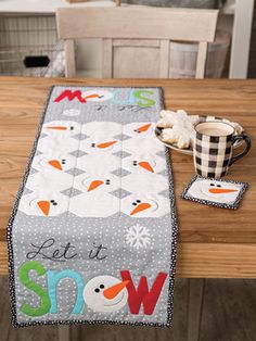 the table runner has snowmen on it and is next to a cup with coffee