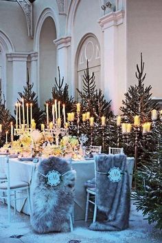 a dining room table is set with candles and christmas trees in the background, surrounded by snow - covered chairs