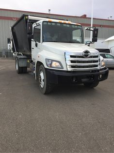 a white dump truck parked in front of a large building with other trucks behind it