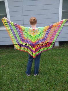 a woman standing in the grass holding a colorful shawl over her shoulders and back