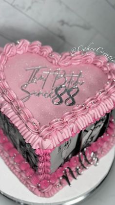 a heart shaped cake with pink frosting and black writing on the top is sitting on a white plate