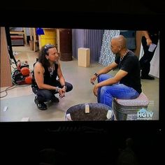 two men are sitting on the floor talking to each other in front of a television screen