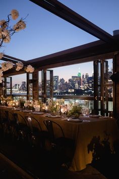 a long table is set with flowers and candles in front of the cityscape