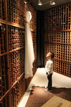 a little boy standing in front of a dress hanging on a rack full of wine bottles