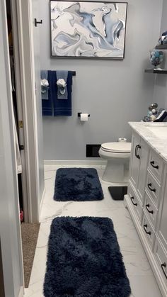 a bathroom with two blue rugs on the floor and a painting above the toilet