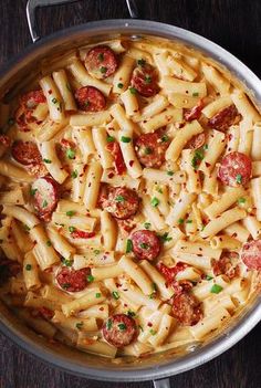 a pan filled with pasta and sausages on top of a wooden table next to utensils