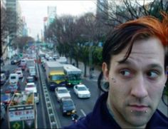 a man with red hair and piercings standing in front of a busy city street