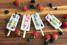 three popsicles with fruit on them sitting on top of a wooden table next to berries and strawberries