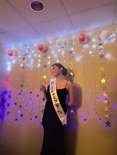 a woman in a black dress holding a wine glass and standing next to a wall decorated with stars