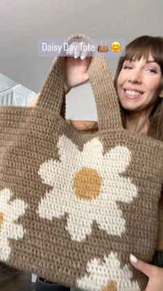 a woman holding up a crocheted bag with daisies on it