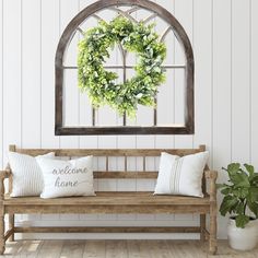 a wooden bench sitting under a window with a wreath on it