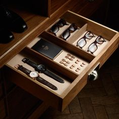 an open drawer with several pairs of glasses, watch and other items in it on a wooden table