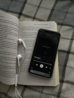 an open book with headphones laying on top of it next to a cell phone