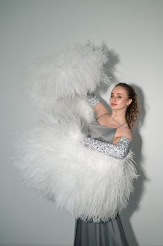 a woman in a dress is posing with a large white feathered object on her arm