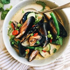 a bowl filled with mussels and vegetables on top of a white table cloth