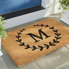 a door mat that has the letter m on it next to a potted plant