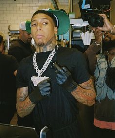 a man in black shirt and gloves holding a camera next to another man with tattoos on his arm