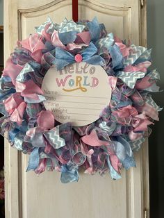 a pink and blue wreath with the words hello world on it hanging from a door